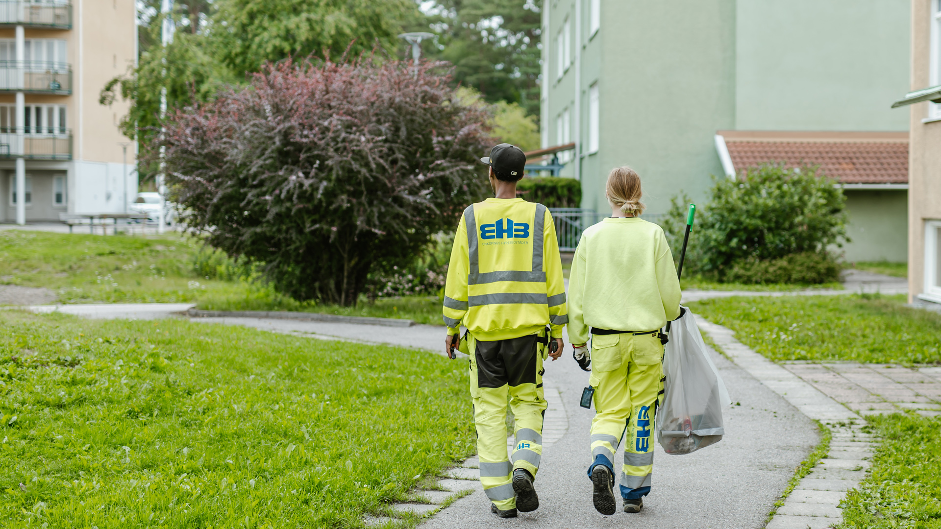 Två sommarjobbare som går i ett bostadsområde och plockar skräp