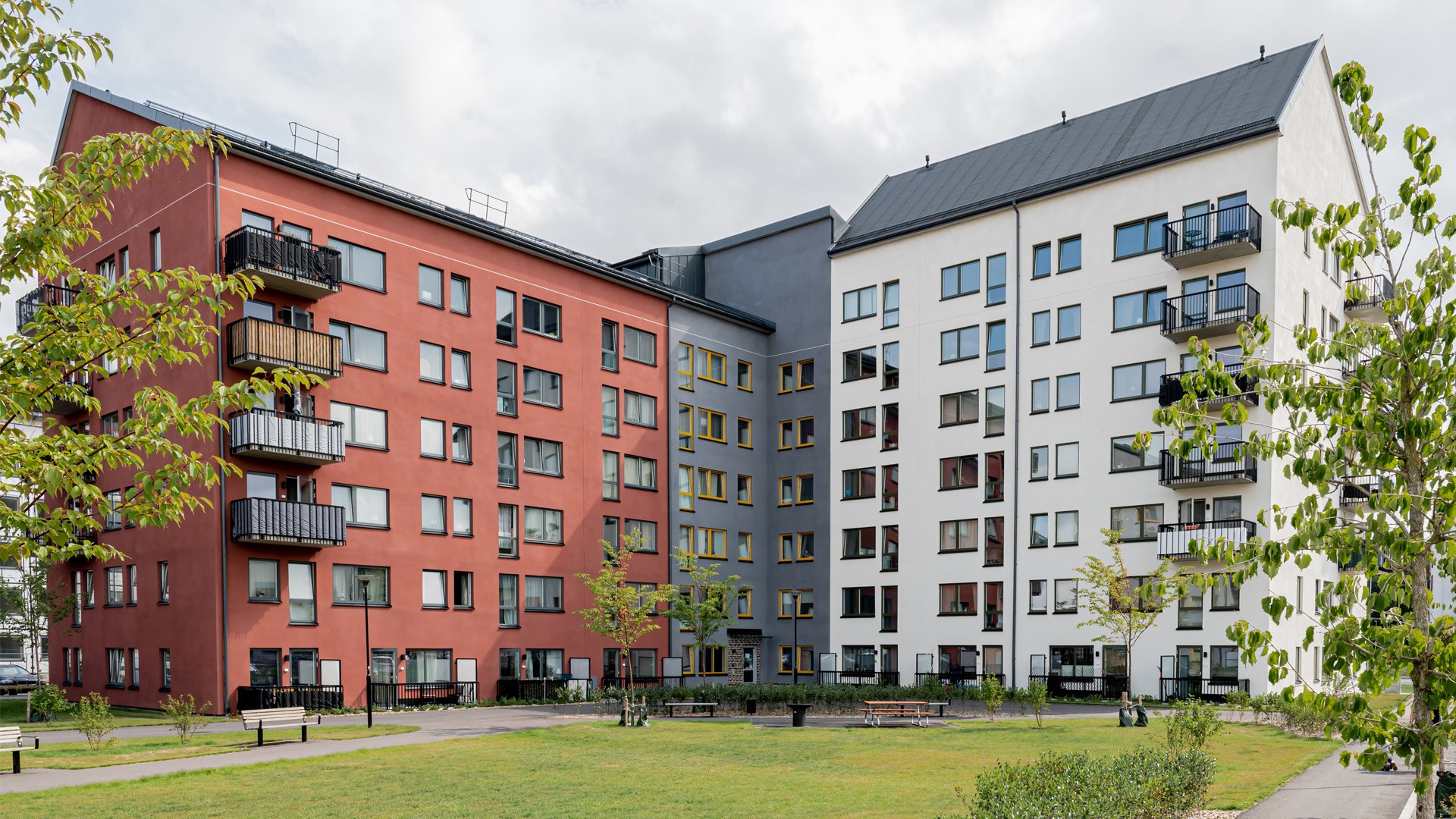 Flerbostadshus i vinkel i flera våningar. Fasad i rött, grått och vitt.