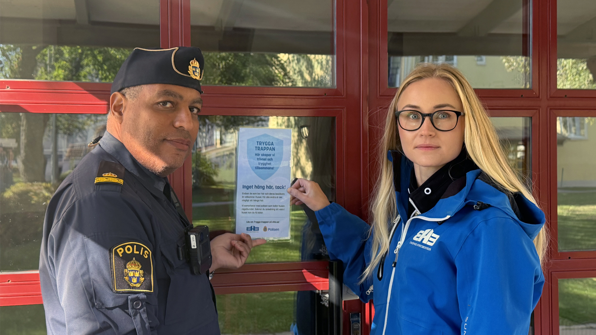 En polis och medarbetare från EHB framför en entré med en lapp uppsatt