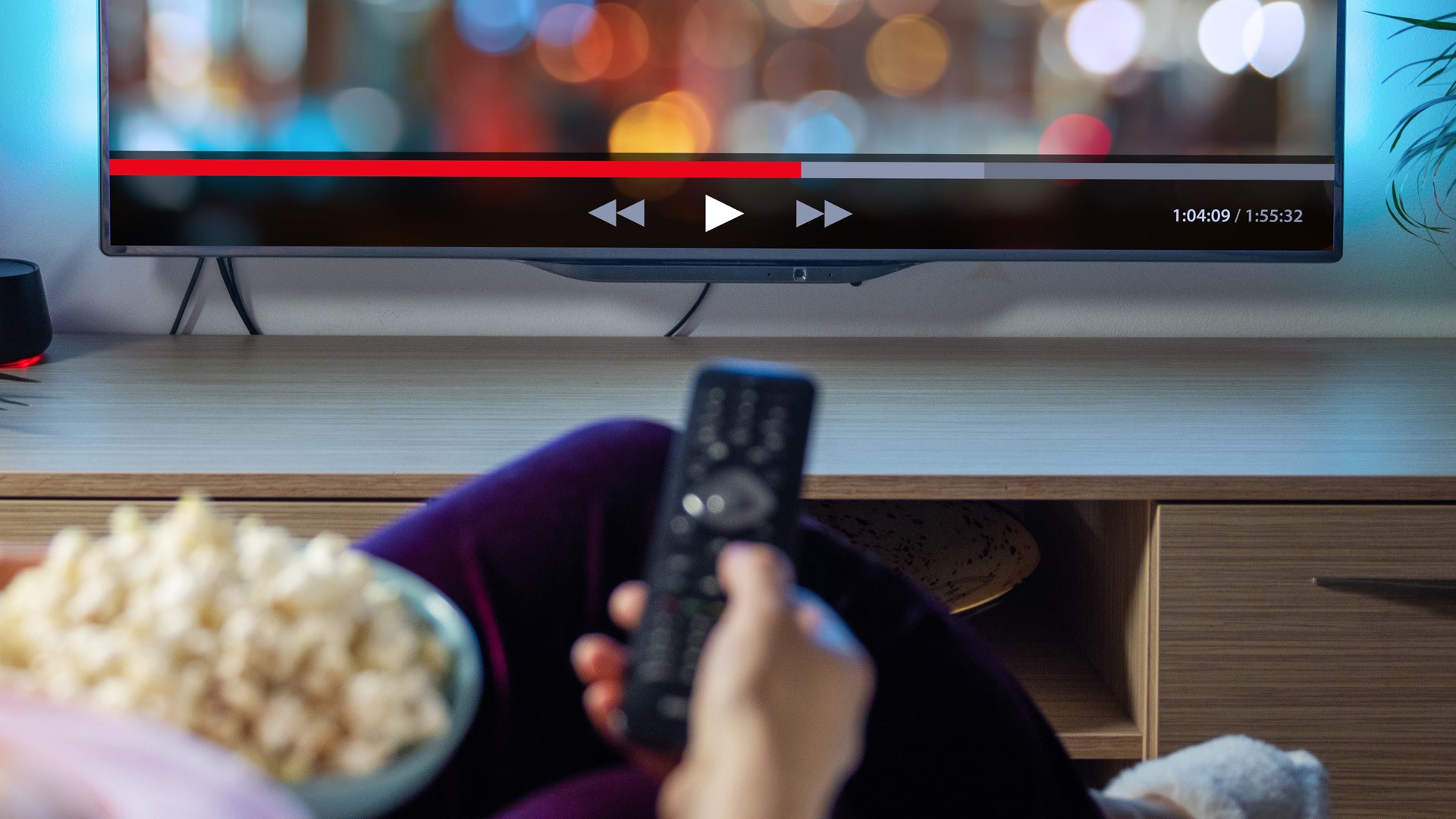 En kvinna sitter med en skål popcorn och håller i fjärrkontrollen till tv:n