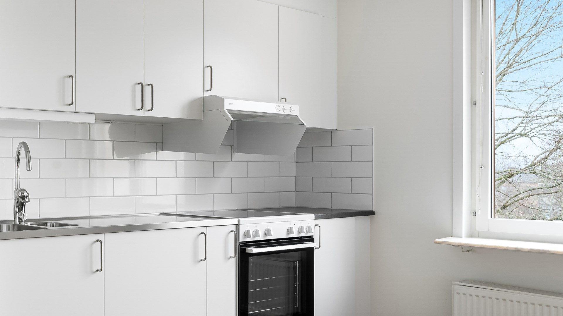 Kök med vita köksluckor, vitt kakel som stänkskydd, vitmålade väggar